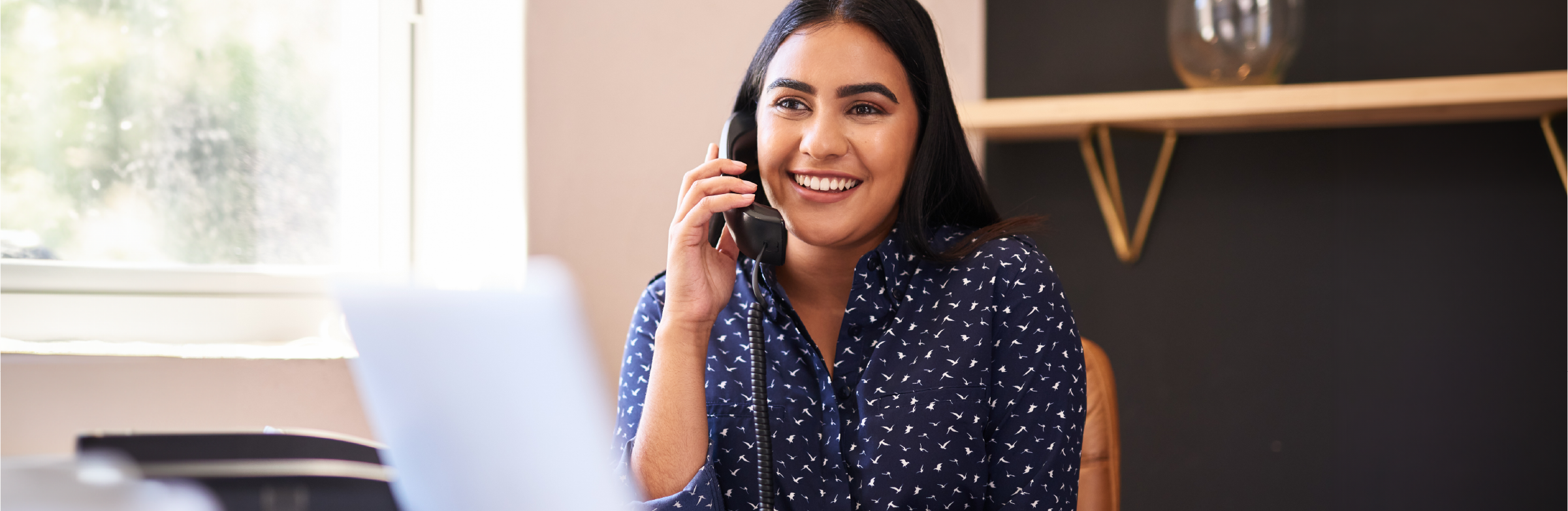 Administrative Assistant working on a laptop while smiling and talking on the phone.