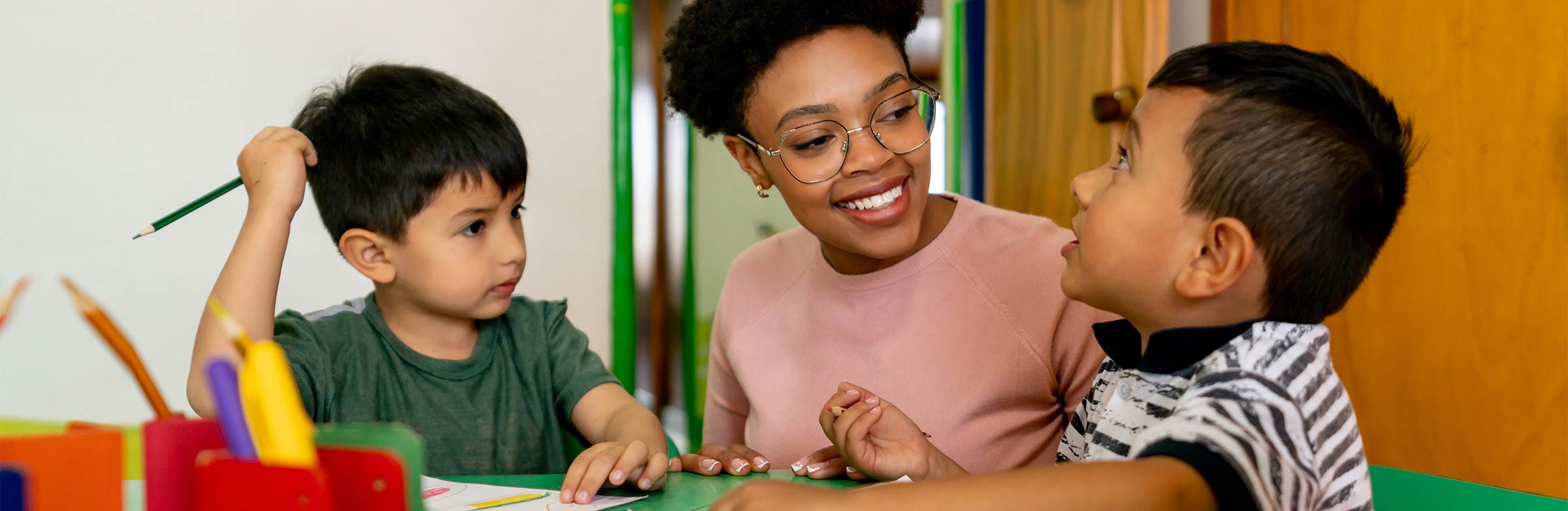 An early childhood educator works with two young children on a worksheet.