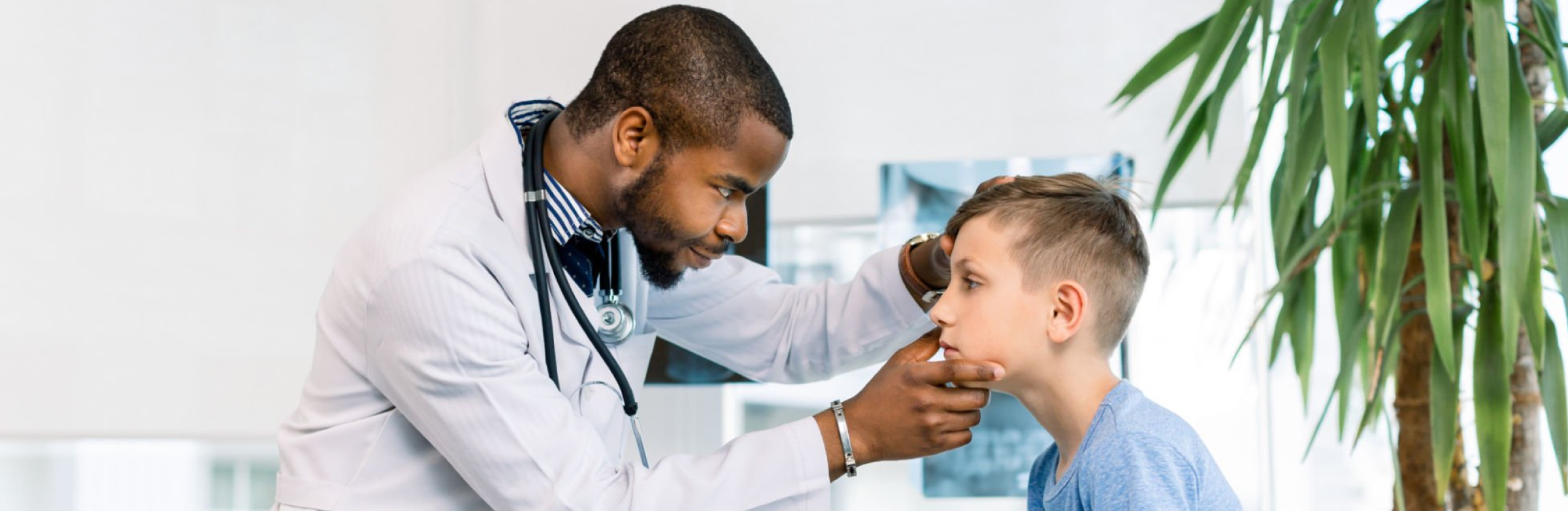 A male doctor examines a young boy’s eye in a clinic setting.